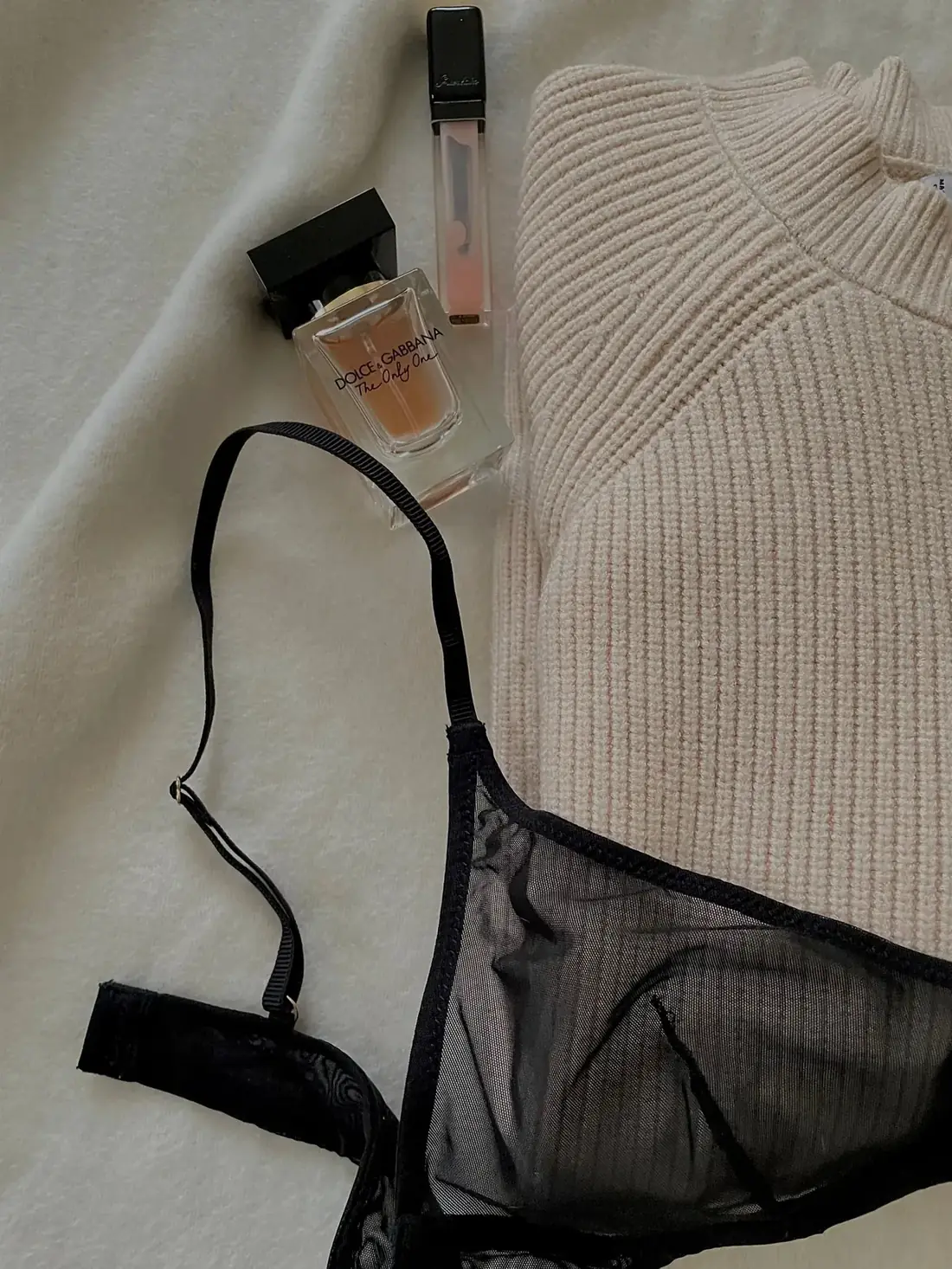 Black bra and neutral knitwear arranged in a product-style flat lay