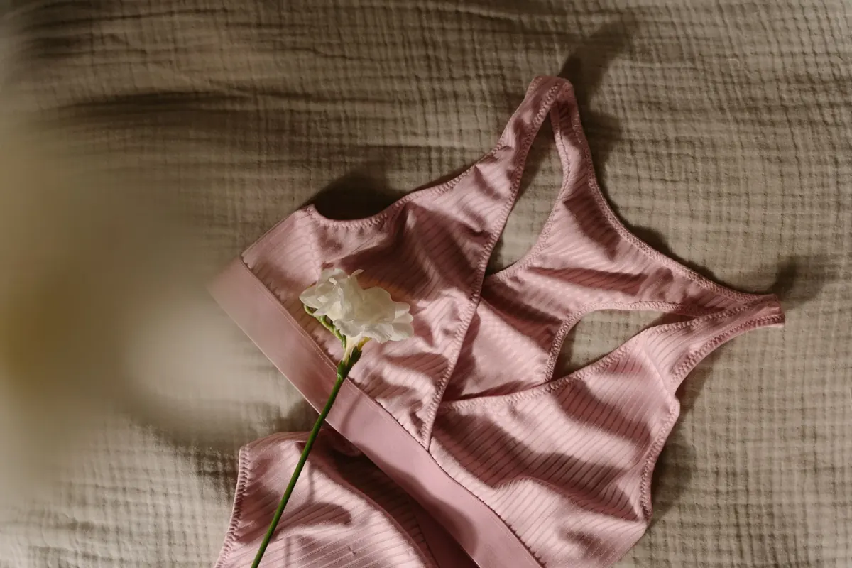 Soft pink sports bra arranged on a bed with a simple flower accent
